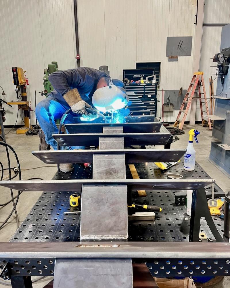 Welder working on a steel staircase frame in the shop, showcasing precision welding and craftsmanship during the fabrication phase for a custom staircase project in San Luis Obispo.